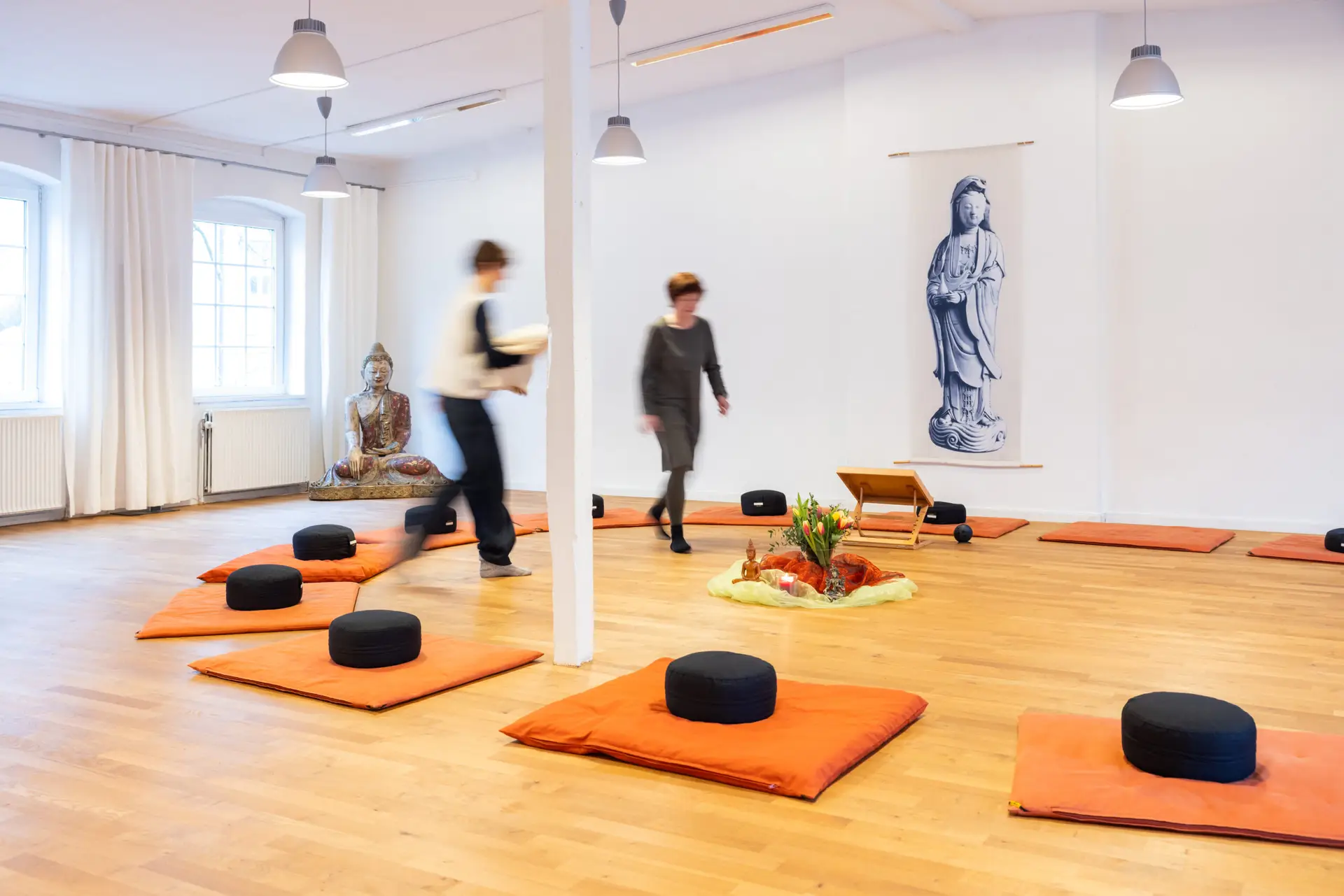 Meditationsraum mit Sitzkissen, Blumen und Buddhafigur.