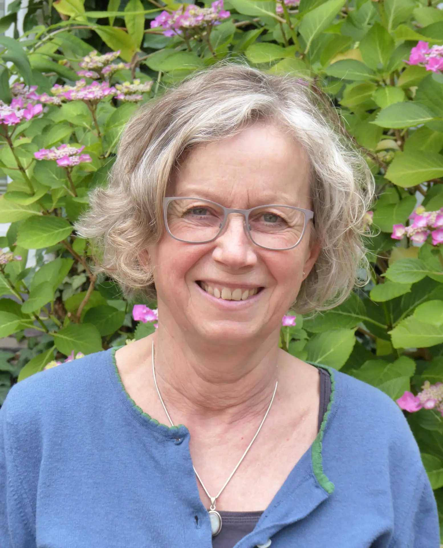 Lächelnde Frau mit Brille vor Blumen.