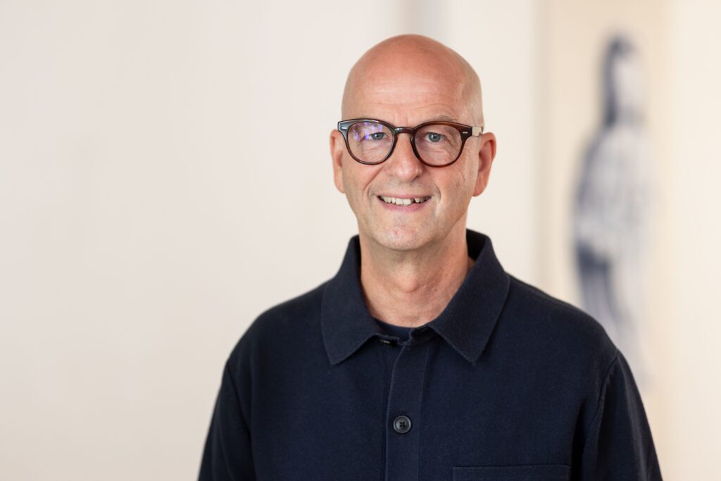 Lächelnder Mann mit Brille vor hellem Hintergrund.